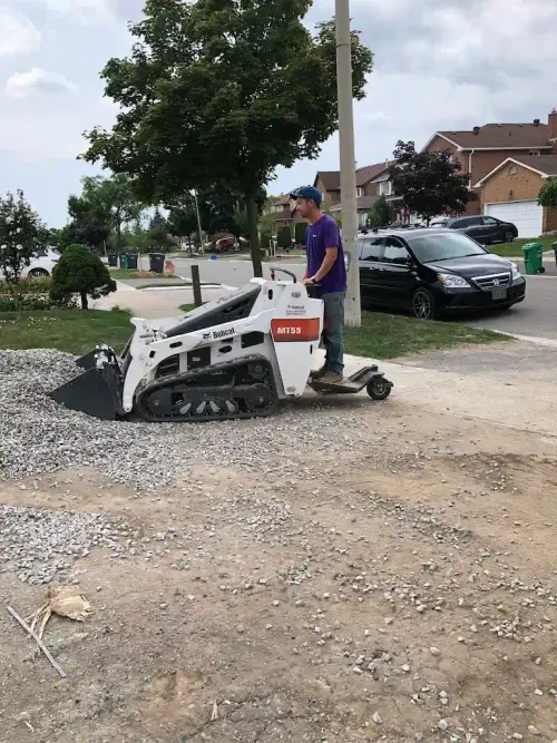 Worker driving a mini track loader over gravel in a driveway