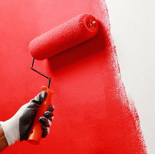 Gloved hand rolling bright red paint onto a white wall