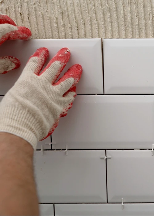 Gloved hand pressing a white subway tile into adhesive