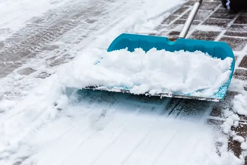 Blue snow shovel clearing snow from a paved walkway