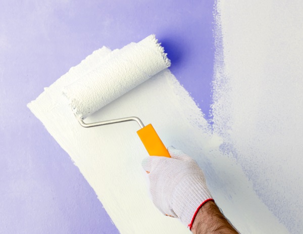Gloved hand rolling white paint over a purple wall