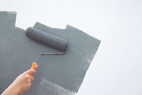 Hand rolling dark grey paint onto a white wall