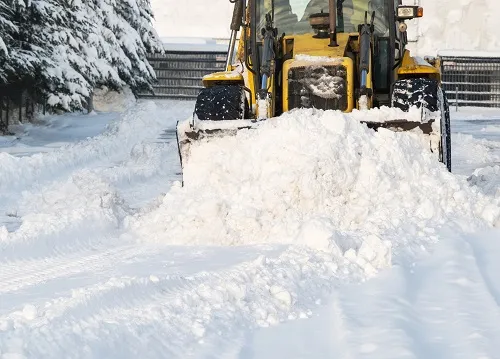 Yellow loader pushing snow along a snow-covered lane